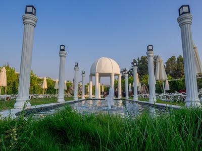Symmetrischer Garten mit weißer Kuppel und Säulen unter klarem Himmel.