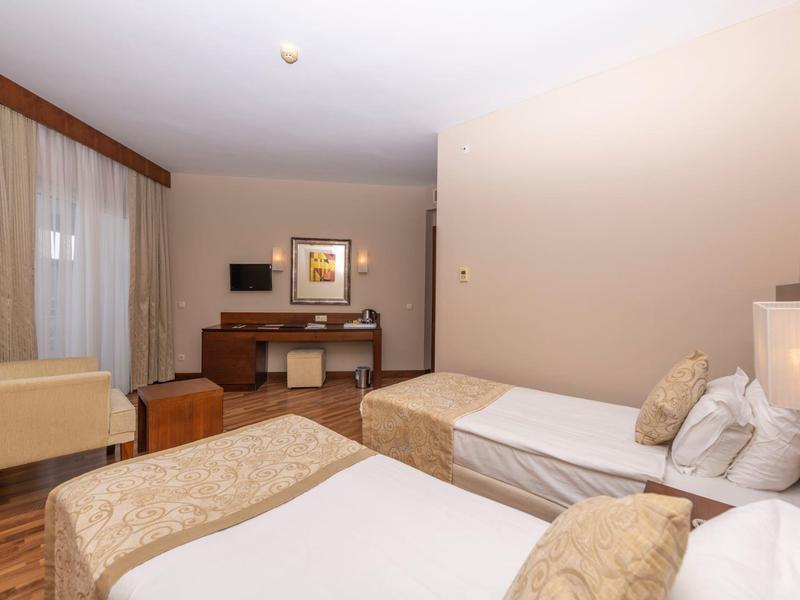 Camera d'hotel con due letti singoli, scrivania, sedie e illuminazione calda.