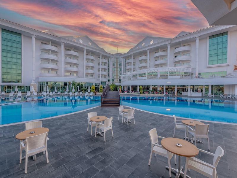 Zona piscina di un hotel moderno con tavoli, sedie e tramonto colorato.