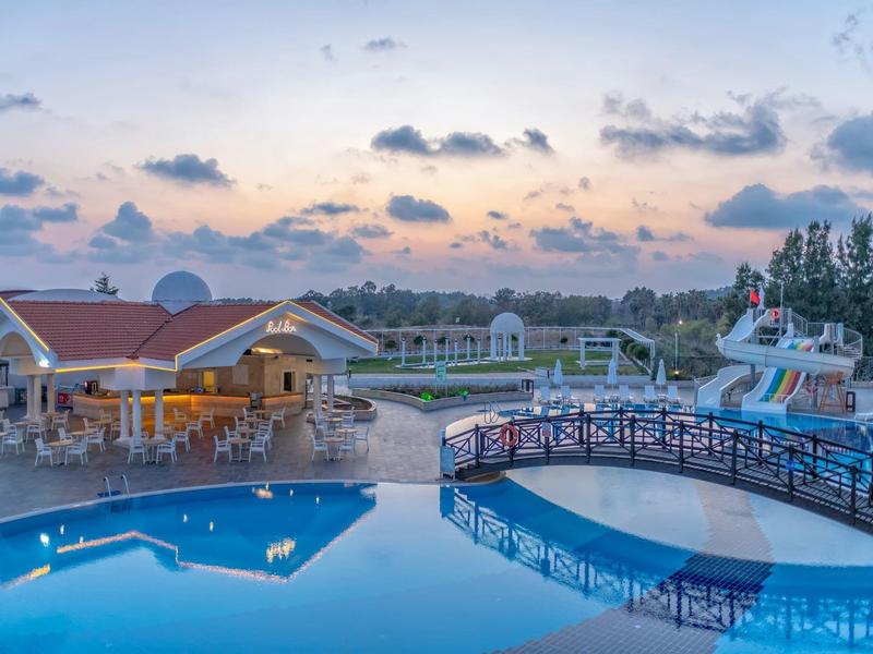 Vista serale di una piscina d'hotel illuminata con scivolo e ponte al tramonto.
