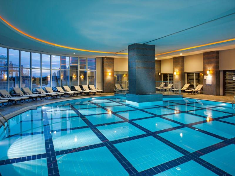 Piscina interna moderna con lettini e ampia finestra che dà all'esterno.