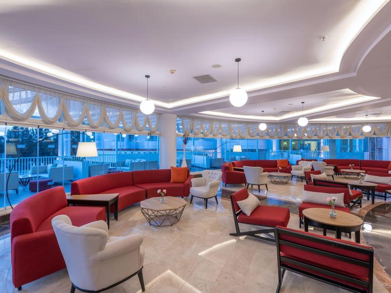 Sala lounge dell'hotel moderna con poltrone rosse e bianche e grandi finestre.