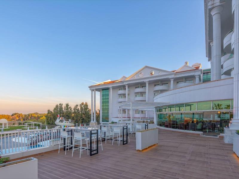 Terrazza con tavoli e sedie, vista su piscina e edificio dell'hotel al tramonto.