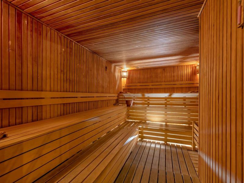 Sauna illuminata con rivestimento in legno e panche in legno a più livelli.