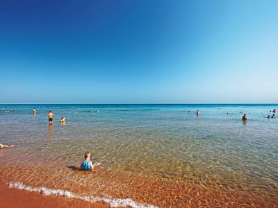 Strand met glad zand en kalm, helder water onder een blauwe hemel