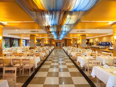 Elegancka restauracja z białymi nakryciami stołów i niebieskim oświetleniem sufitowym.