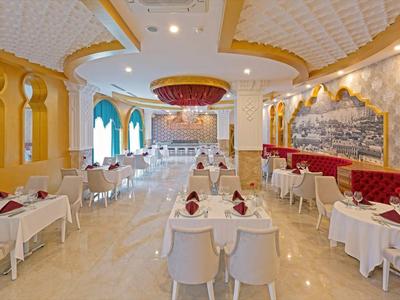 Elegancka, jasna restauracja z białymi stołami i żółtymi ścianami ozdobionymi obrazami.