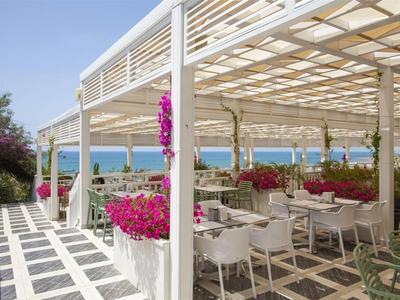 Taras z białą pergolą i kolorowymi kwiatami z widokiem na morze w słoneczny dzień.