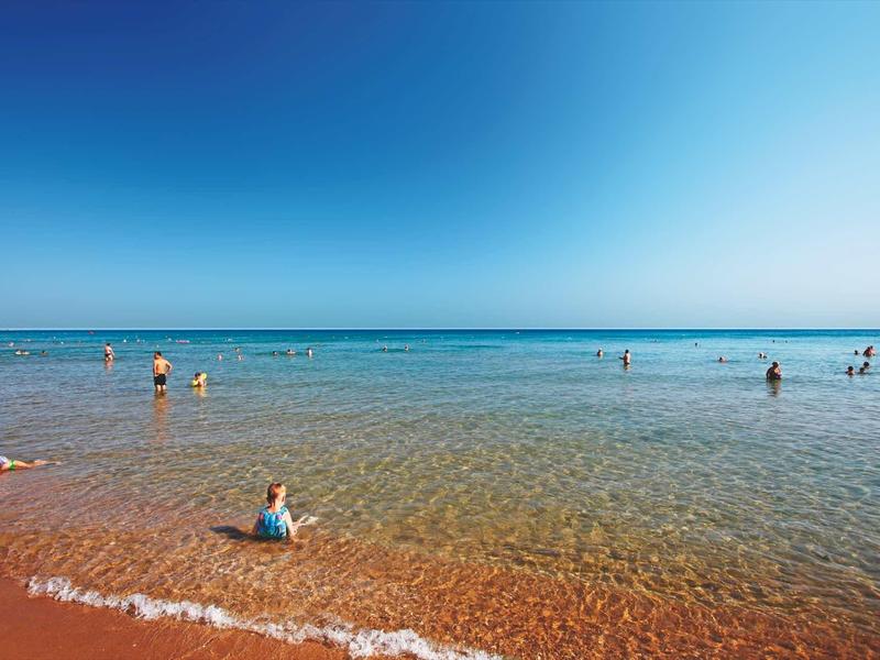 Plaża z czystą wodą i niebieskim niebem, ludzie korzystają z płytkiej wody.