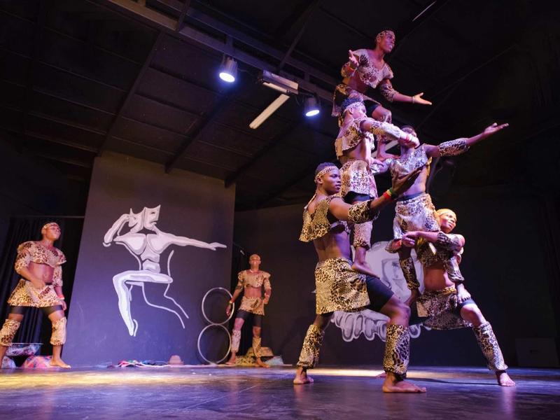 Grupa akrobatycznych tancerzy tworzy piramidę na scenie z dramatycznym oświetleniem.