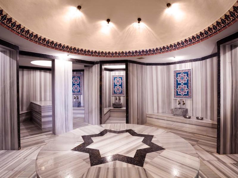 Eleganckie okrągłe pomieszczenie z marmurowymi ścianami, kolumnami i wzorem gwiazdy na podłodze.