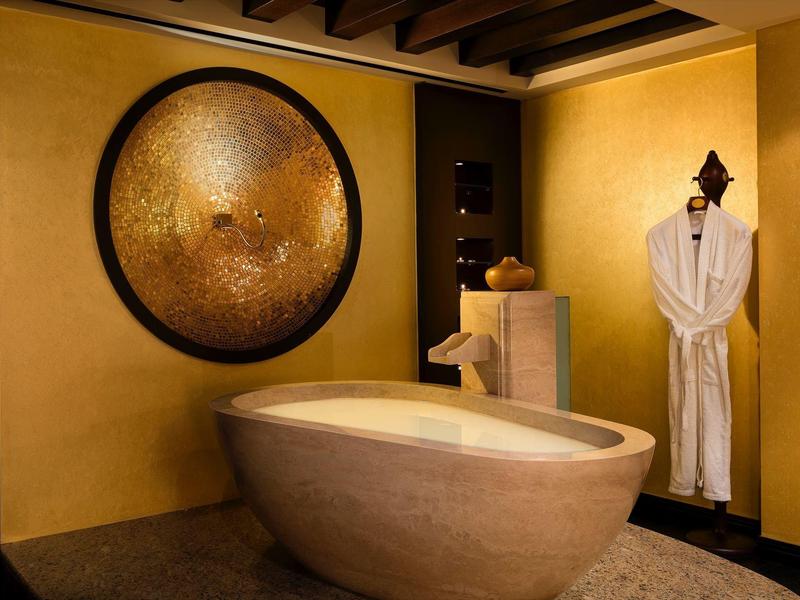 Elegancka łazienka z owalną wanną i okrągłą, złotą dekoracją na ścianie.