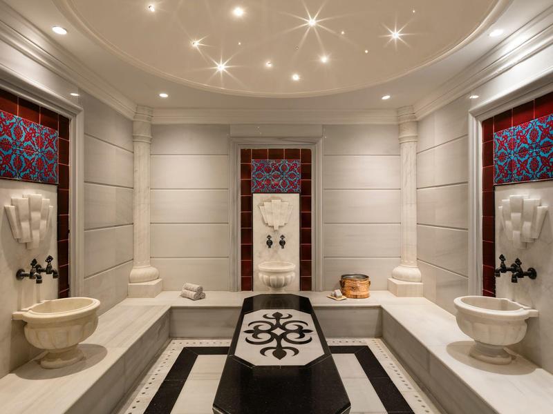 Wnętrze eleganckiego hammamu z marmurowymi ścianami i rzeźbionymi umywalkami.