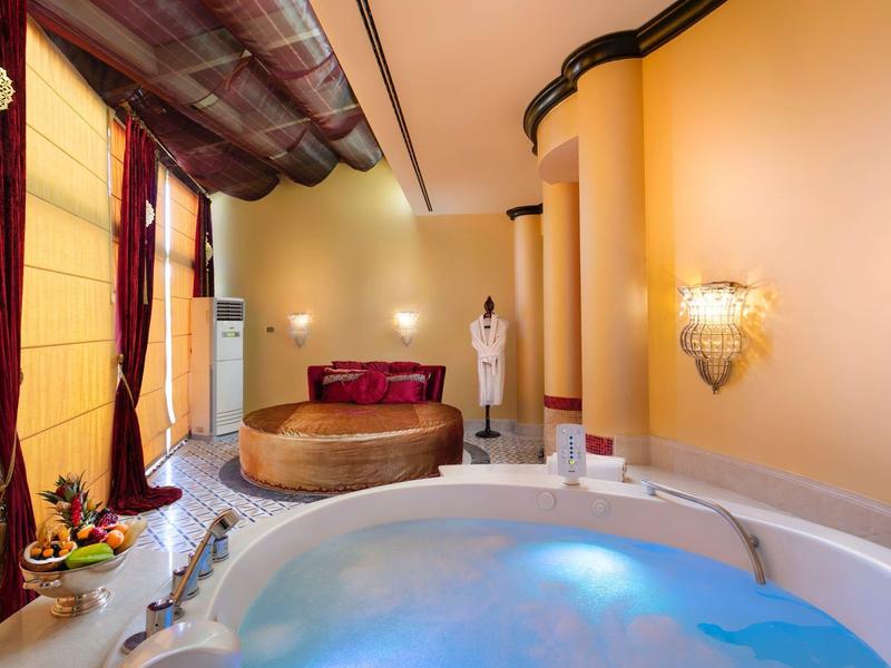 Luksusowy pokój hotelowy z wanną z hydromasażem i okrągłym łóżkiem przy dużych oknach.