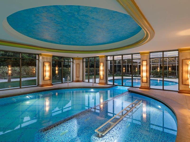 Nowoczesny kryty basen z niebieskim sufitem i dużymi oknami z widokiem na zewnątrz.