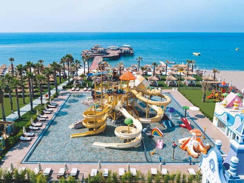 Park wodny z zjeżdżalniami, basenem, leżakami i widokiem na morze i molo.