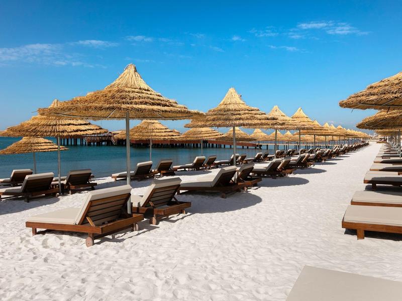 Słoneczna plaża z leżakami i słomianymi parasolami nad morzem.