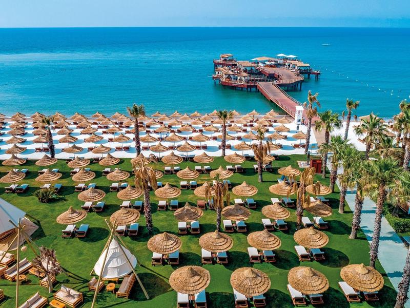 Piaszczysta plaża z parasolami i molo sięgającym turkusowego morza.