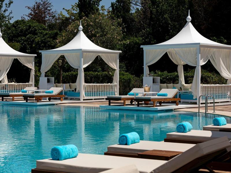 Basen z leżakami i białymi namiotami do relaksu na tle zieleni.