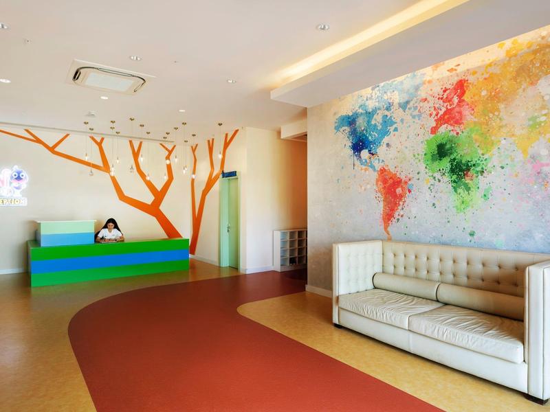 Kolorowa recepcja hotelowa z mapą świata na ścianie i białą sofą.