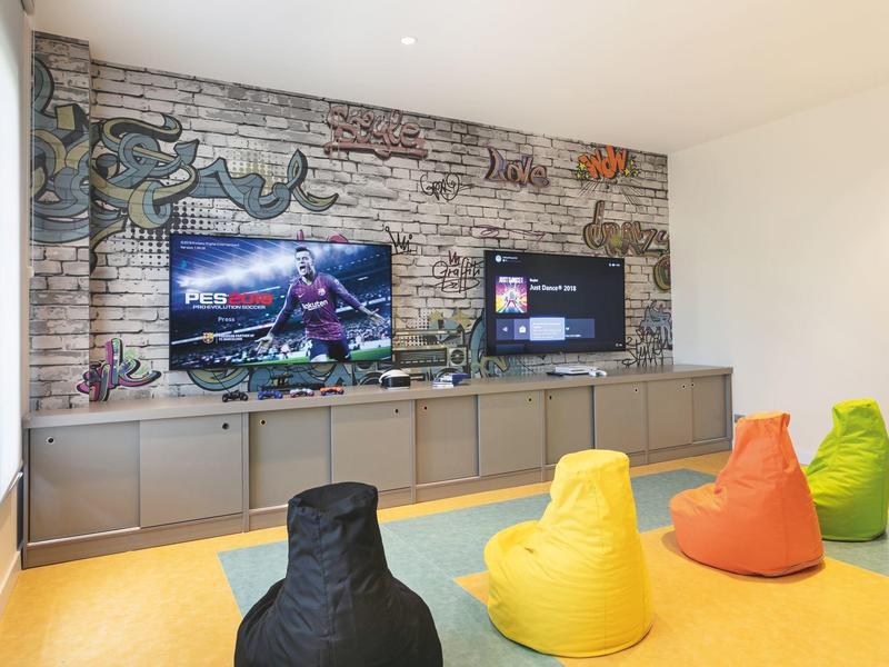 Pokój rozrywki z telewizorami na ścianie i kolorowymi siedziskami worekowymi.