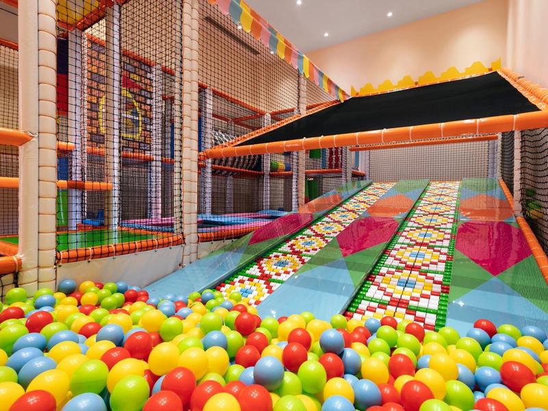 Kolorowy, kryty plac zabaw z basenem z piłeczkami i konstrukcjami do wspinaczki.