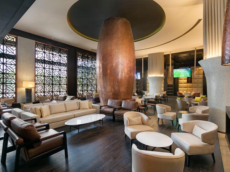 Elegancki salon hotelowy z białymi fotelami, dużą drewnianą kolumną i dużymi oknami.