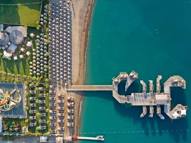 Widok z lotu ptaka na plażę z parasolami, pomostem i strukturami na wodzie w kształcie skorpiona.