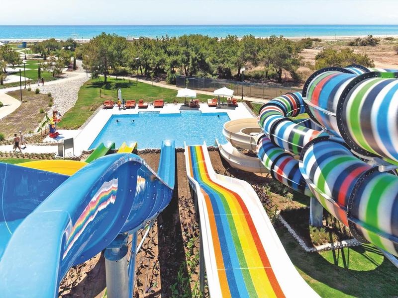 Bunte Wasserrutschen führen zu einem großen Pool mit Palmen und Strand im Hintergrund.