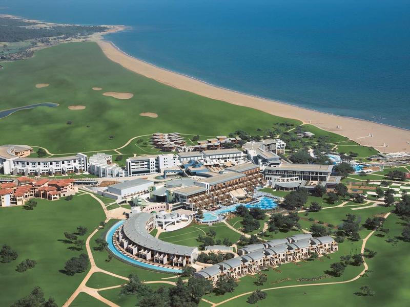 Große Küstenanlage mit Hotels, Pools und einem langen Sandstrand an blauem Meer.