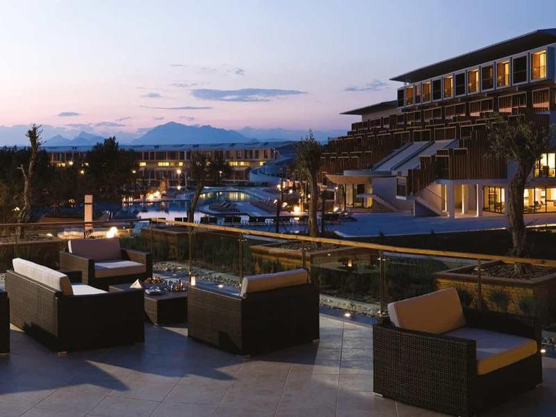 Terrassenbereich mit Sitzgruppen vor modernem Hotelgebäude bei Dämmerung, sanfte Beleuchtung.