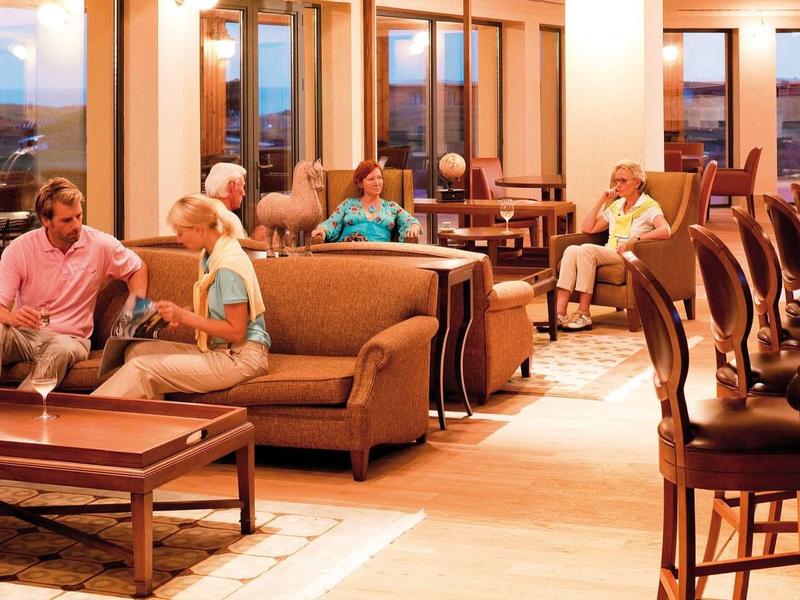 Gemütliche Hotel-Lobby mit Sofas, Tischen und hohen Barhockern, warm beleuchtet bei Sonnenuntergang.