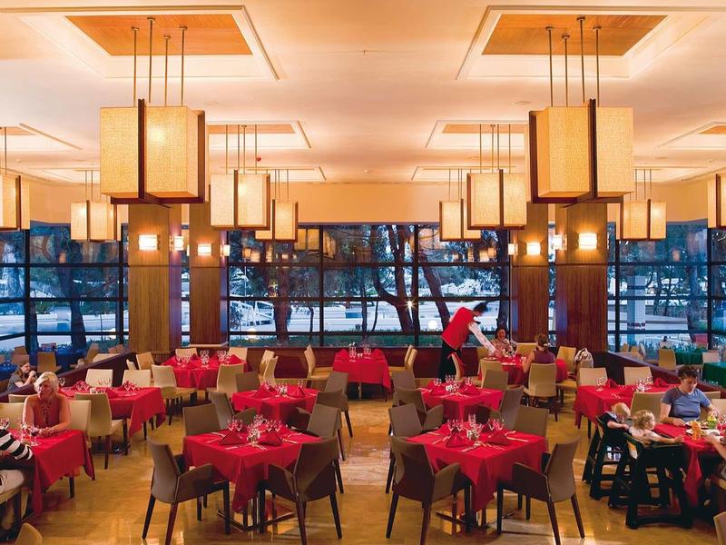 Großes Restaurant mit vielen Tischen, roten Stühlen und modernen, warmen Hängelampen.