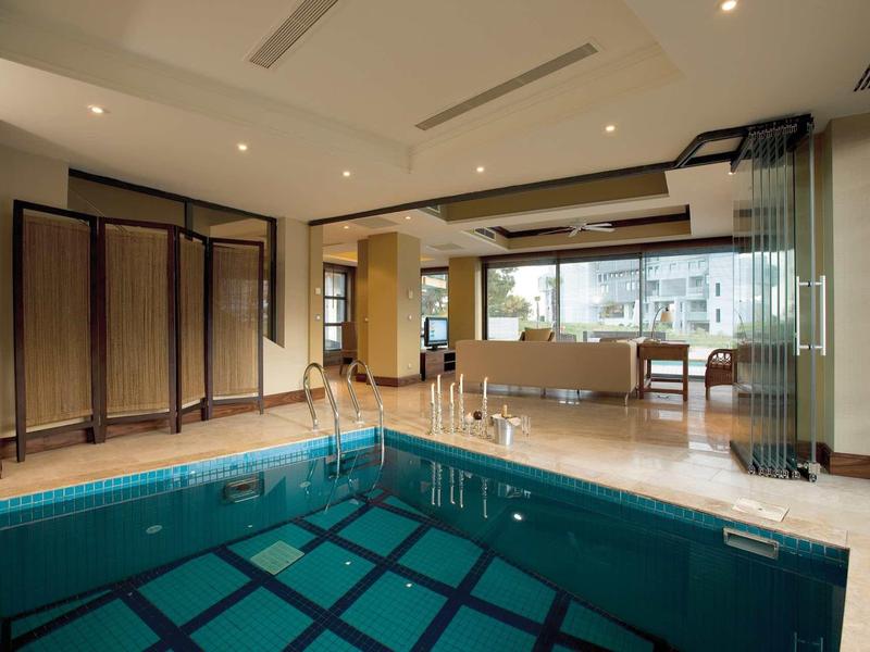 Moderner Indoor-Poolbereich mit Becken, großen Fenstern und Sitzbereich in warmen Naturfarben.