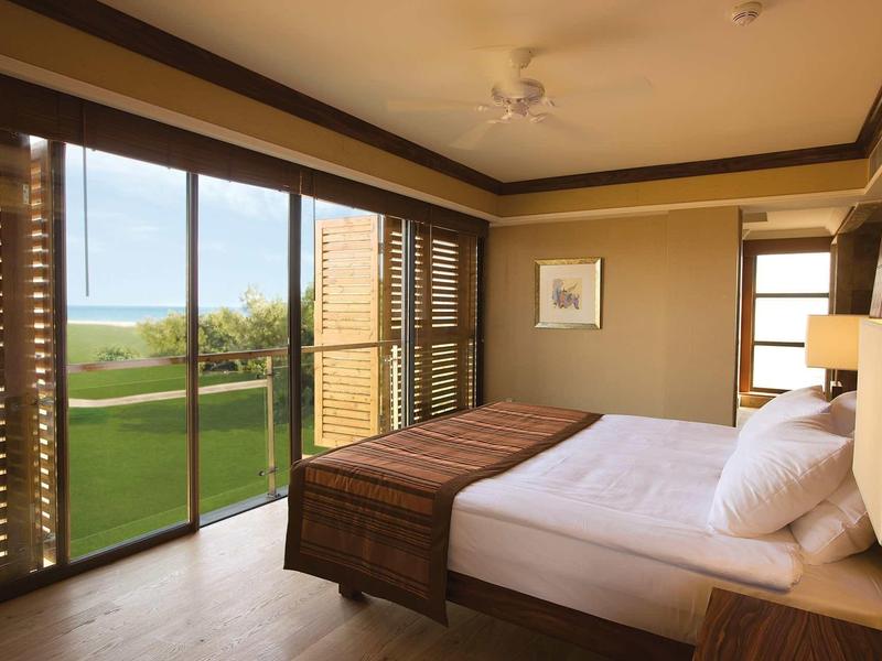 Helles Schlafzimmer mit großem Bett, Holzmöbeln und Panoramafenstern mit Blick auf Grünfläche.