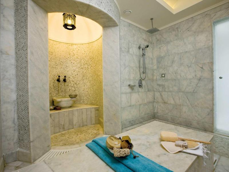 Modernes Badezimmer mit Marmorwänden, begehbarer Dusche und dekorativem Ablagebereich.