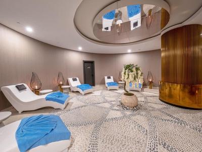 Okrągły pokój wellness z wygodnymi białymi leżakami, niebieskimi ręcznikami i ciepłym oświetleniem.