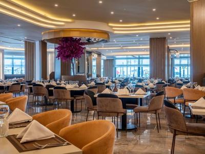 Elegancka restauracja hotelowa z nakrytymi stołami, wygodnymi krzesłami i nowoczesnym oświetleniem.