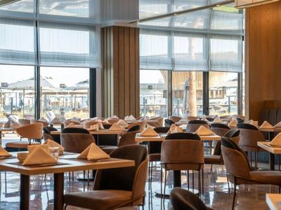 Nowoczesna restauracja hotelowa z nakrytymi stołami i dużymi oknami z widokiem na miasto.