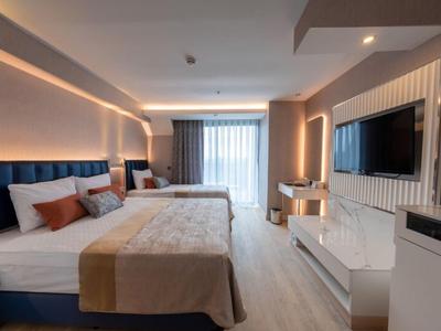 Modern hotelkamer met twee bedden, tv en groot raam met gordijnen.