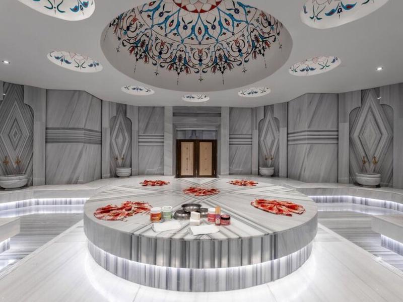 Nowoczesny hammam z okrągłą marmurową fontanną i ozdobnym malowidłem sufitowym.