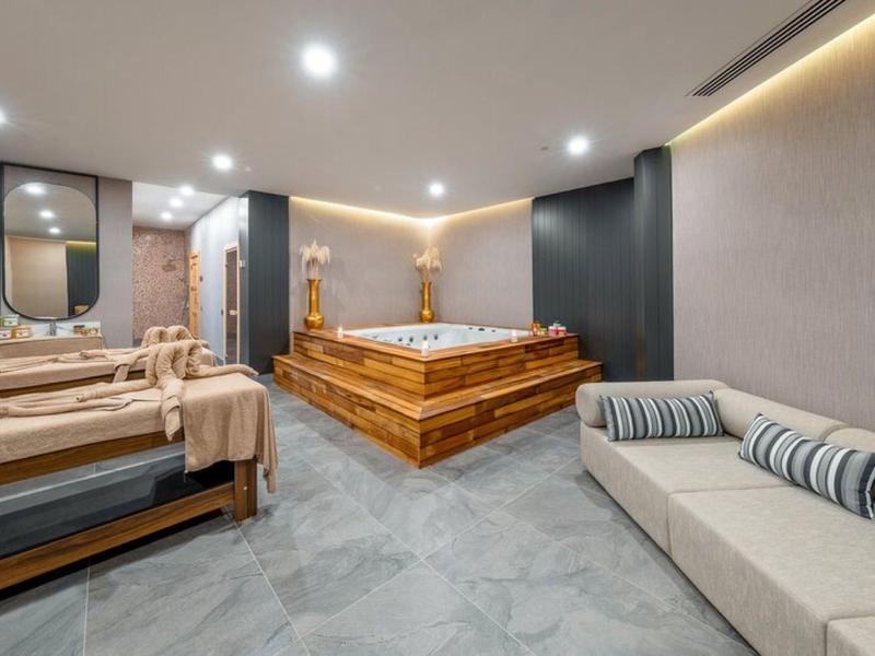 Nowoczesny pokój spa z jacuzzi, leżankami do masażu i sofą w neutralnych kolorach.