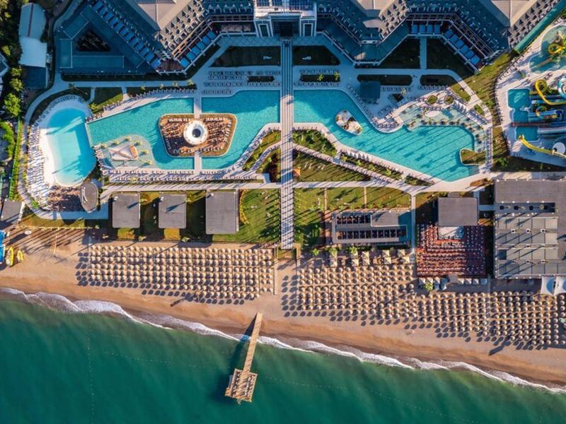 Widok z lotu ptaka na ośrodek z wieloma basenami, parasolami i bezpośrednim dostępem do plaży.