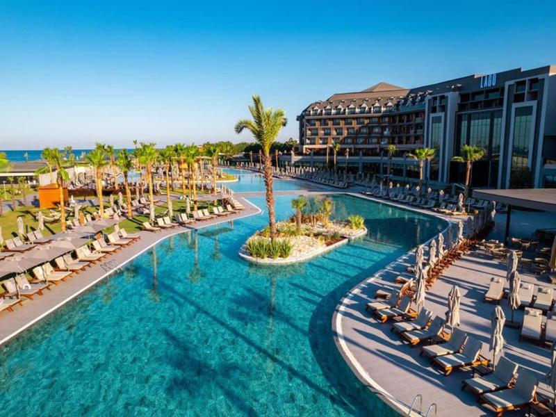 Luksusowy ośrodek hotelowy z dużym basenem, leżakami i palmami w słoneczną pogodę.