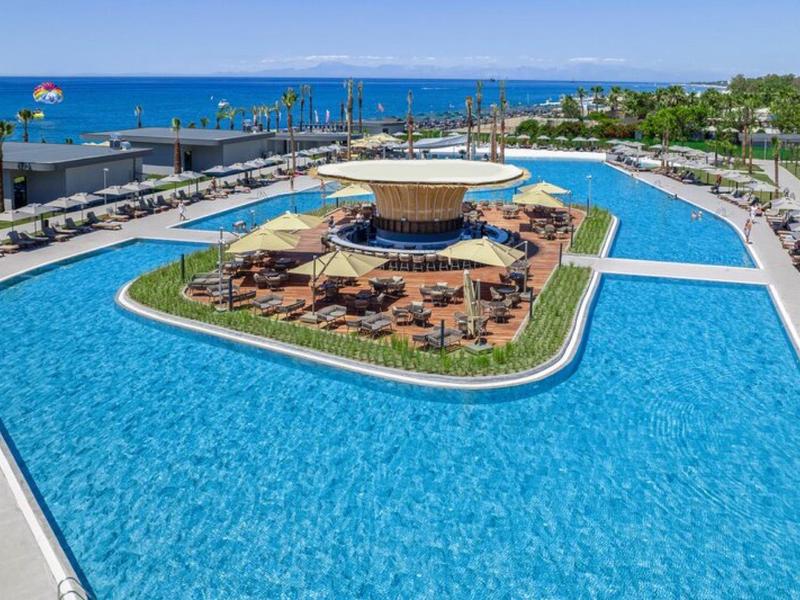 Duży basen hotelowy z barem na wyspie i leżakami blisko morza.