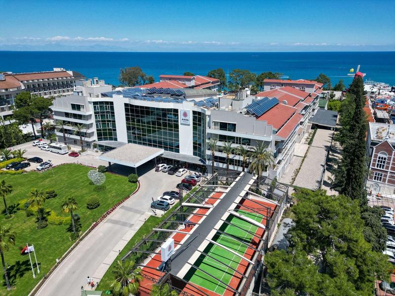 Modern hotel complex near the ocean with glass facade and lush green gardens.