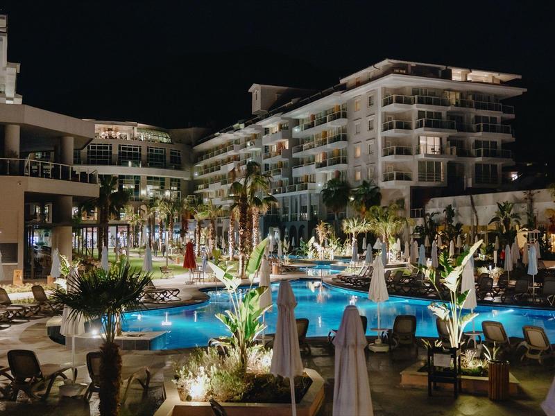 A night view of a lit hotel pool area surrounded by lounge chairs and palm trees.