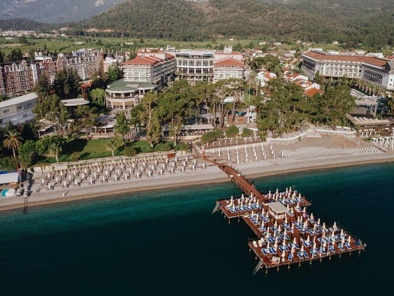 A large beachfront hotel with rows of sunbeds and umbrellas on the beach and a wooden pier extending into the sea.