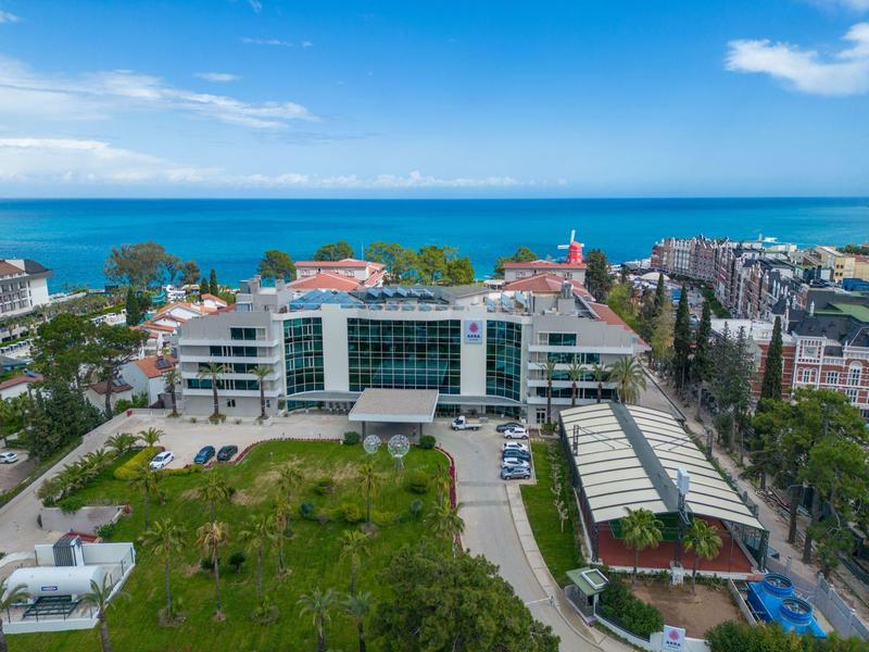 Modern hotel building with glass facade near green lawn and ocean under blue sky.