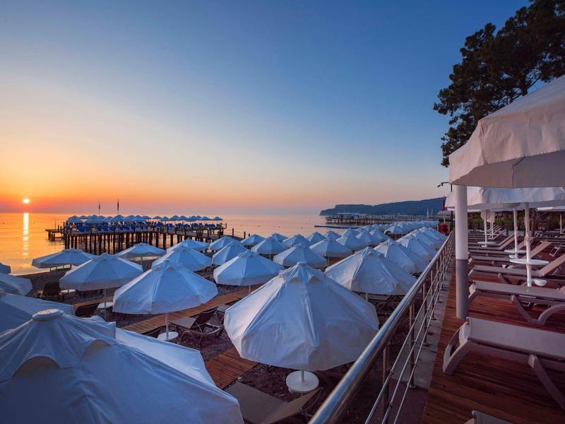 Sunset view of beach umbrellas and lounge chairs on a hotel terrace near the water.